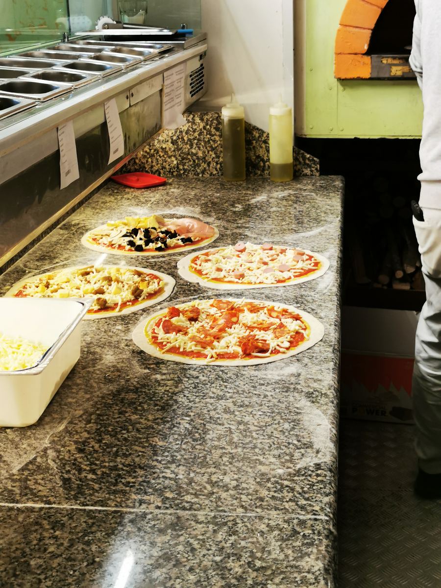 Pizze pronte sul bancone in granito accanto al forno a legna